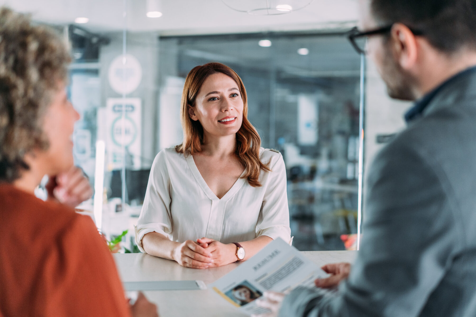 Een opname van een mannelijke recruiter die een vrouwelijke kandidaat interviewt. De sollicitante overhandigt haar cv aan de directeur terwijl ze samen met hem aan tafel zit tijdens het sollicitatiegesprek. Een mannelijke werkgever neemt een cv aan van een sollicitante.